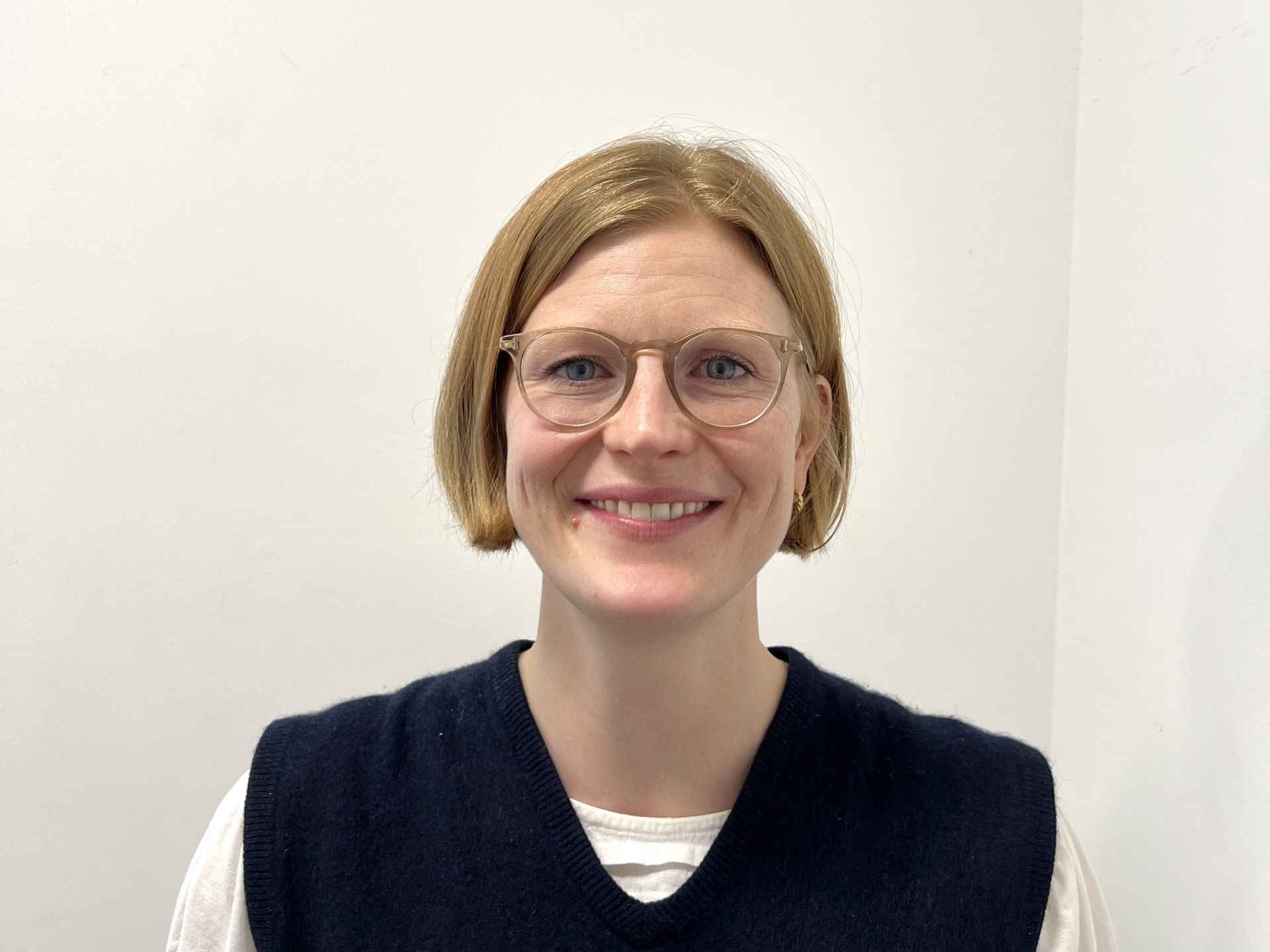 Georgia Stevenson, Head of the Sands and Tommy's Joint Policy Unit, is a white woman with light brown bobbed hair. She is wearing glasses and a white t-shirt under a black knitted top. She is facing the camera and smiling.
