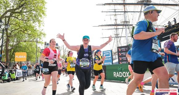 A woman running past a ship, with hands up in the air.