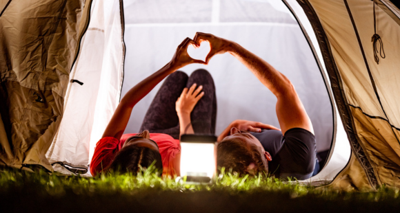picture of two people laid down in their tent, placing their hands together to form a heart 