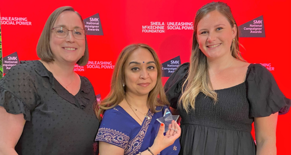 Three people standing together at an awards ceremony, holding awards.