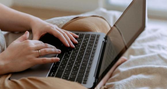 Somebody using their laptop whilst sat on their bed.