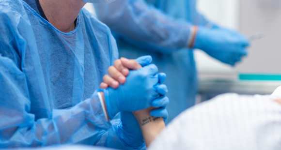 Person in scrubs holds hands with someone lying down