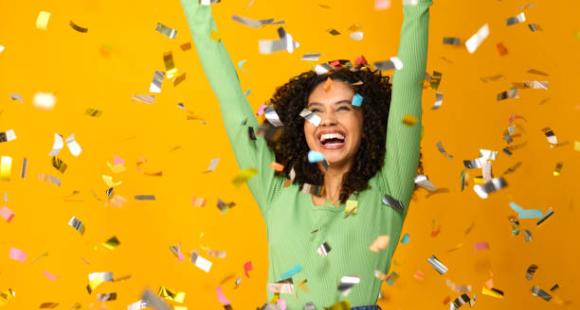 Woman celebrating with her arms in the air. Metallic confetti is showering down on her.