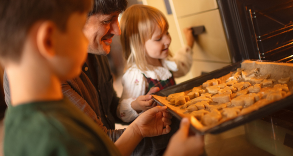Picture showing a dad with 2 children putting some cookies in to the oven