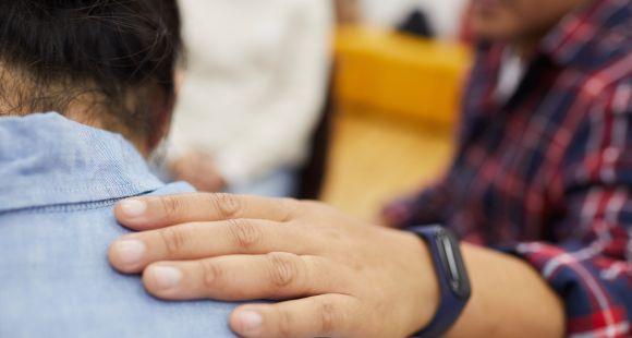 Man with a watch on his wrist has his hand on the back of another man's shoulder