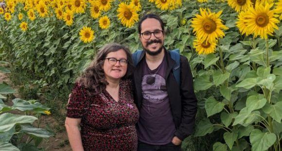 A man and a lady smile at the camera with yellow sunflowers in the badckground behind them following the preventable death of their daughter Smokey in 2023.