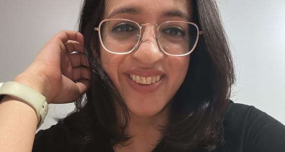 Lady with dark hair and glasses wearing a black top smiling at the camera