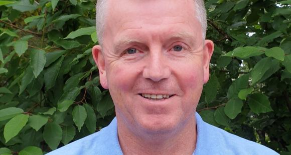 Man with grey hair and a blue t-shirt by a tree