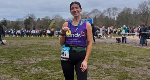 A woman standing in a field holding with her hand a medal.