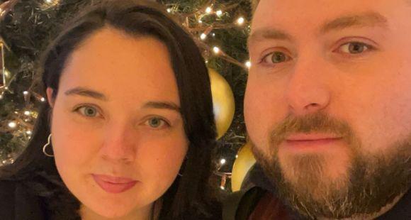 A lady with dark hair and a man with a beard looking at the camera with twinkling tree lights in the background