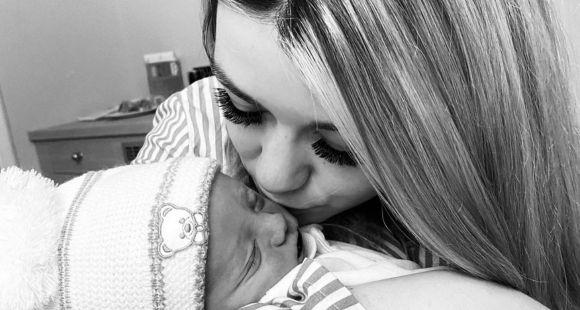 A lady with long blonde hair kissing her baby who has a woolly hat on on his face