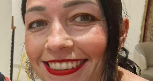 A lady with dark hair wearing red lipstick smiles at the camera