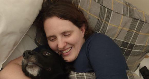 A lady in bed cuddling a black dog