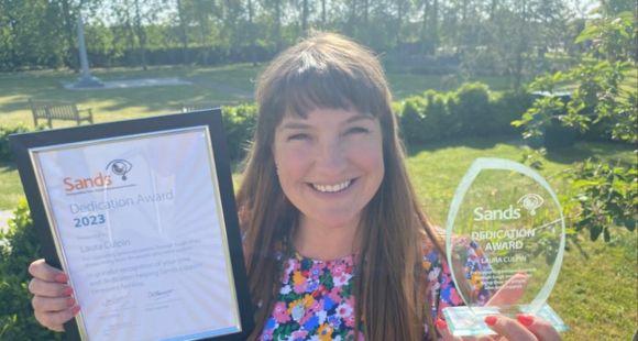 Lady with long dark brown hair holding an award and smiling at the camera