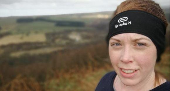 Lady wearing a black running headband with a scenic view in the background smiling at the camera