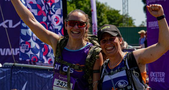 Two ladies in Sands running vests smiling at the camera with hands in the arm running after experiencing multiple miscarriages