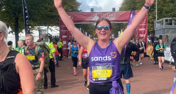 A woman standing up, with arms up in the air, after running a race,