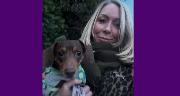 A lady with a blonde bob wearing a scarf smiles at the camera holding a brown mini dachshund