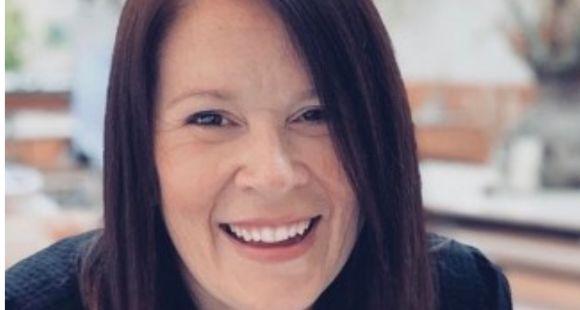 A lady with black hair and a black jacket smiling at the camera