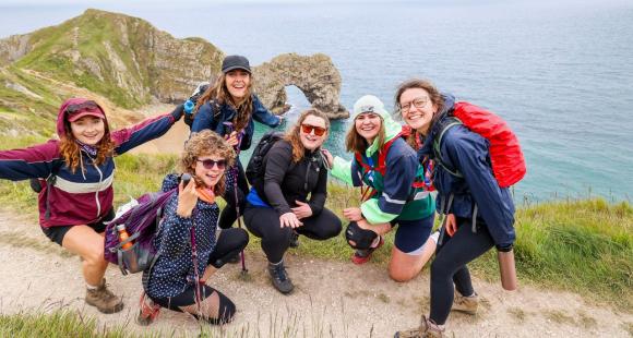 Six women on a path, with the sea and cliffs.