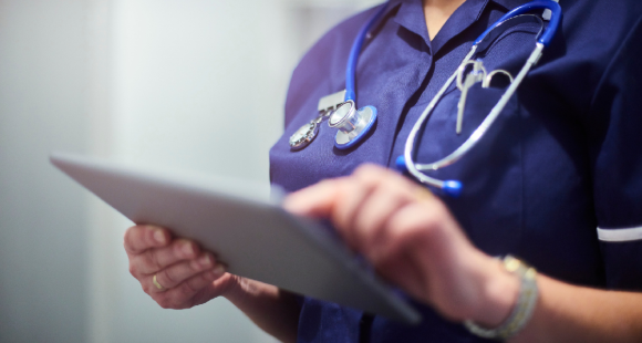 An NHS worker in a dark blue tunic using an electronic tablet