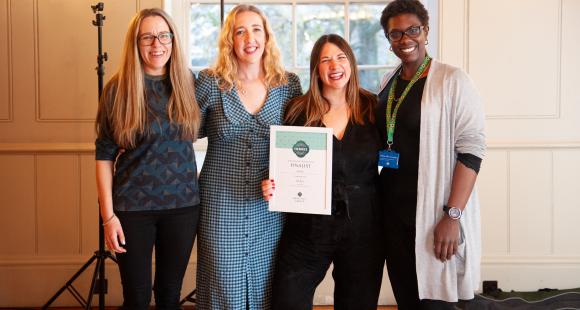 Four ladies stood together, smiling and looking at the camera as they are presented with a certificate