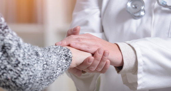 A healthcare professional holding the hand of their patient in compassion