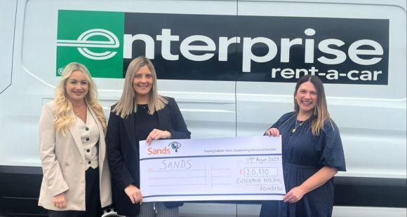 Three ladies stood infront of an Enterprise van holding a large cheque