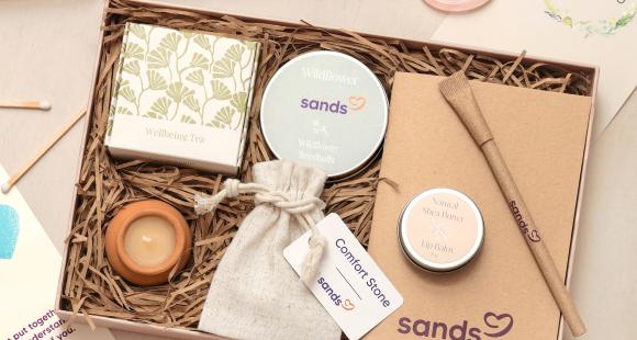 Sands Wellbeing Box pictured with notebook, pen, comfort stone, wildflower seeds, tea, tea light and lip balm