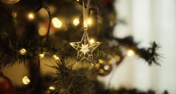 A golden star christmas tree decoration with Sands logo hangs on a beautifully lit Christmas tree.