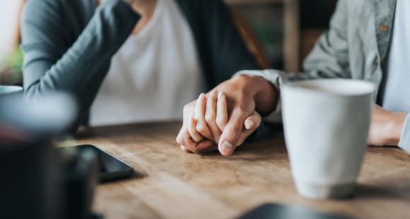 Image of couple holding hands on a table while drinking coffee