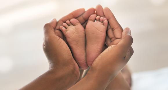 Two adult hands hold a baby's feet