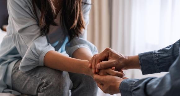 Two people sat down, no faces are in shot, but they are holding hands in a private moment