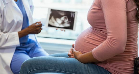 A Black health professional wearing a white coat talks to a Black pregnant woman