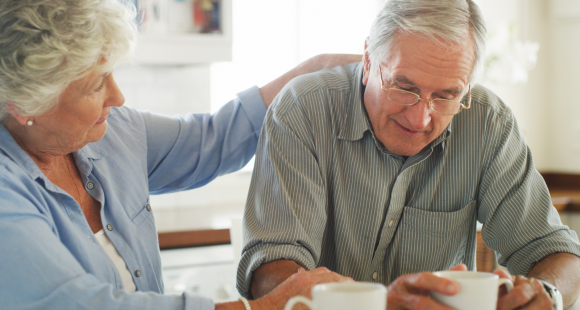 An older woman puts a comforting hand on the shoulder of an older man