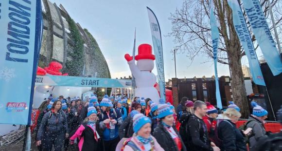 Large crowd of people walking, they are all wearing coats and blue bobble hats. There is a blow up snowman in the background.