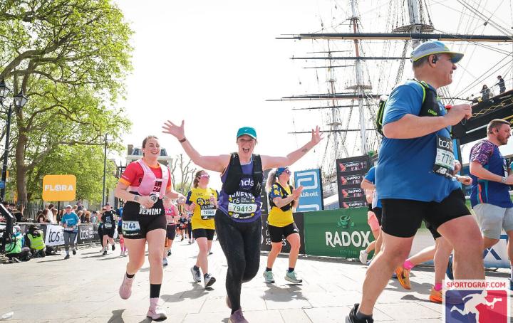 A woman running past a ship, with hands up in the air.