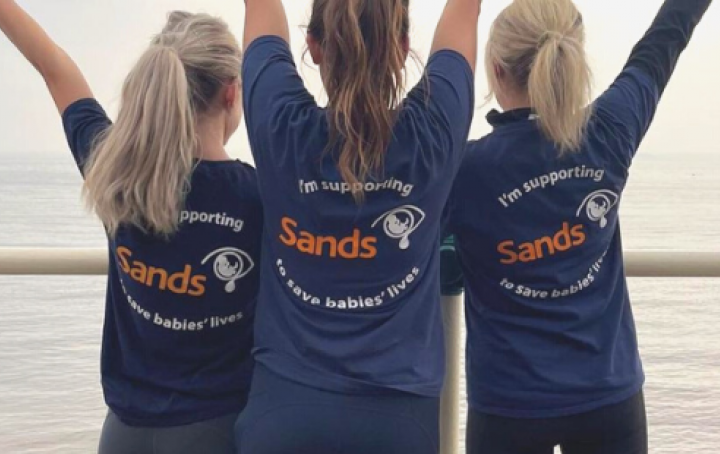Three women wearing Sands t-shirts with the hands in the air