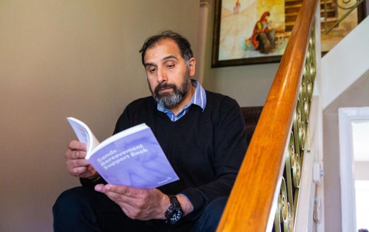 South Asian man sat reading Sands' Bereavement support book