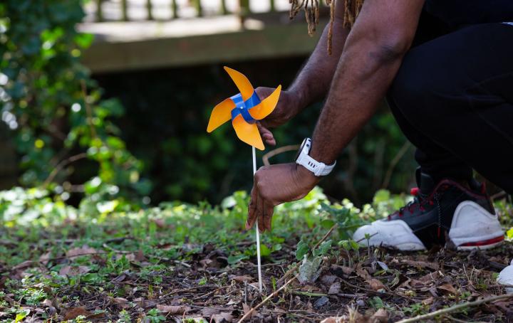 The image of a Black male's hand placing a pinwheel in the ground