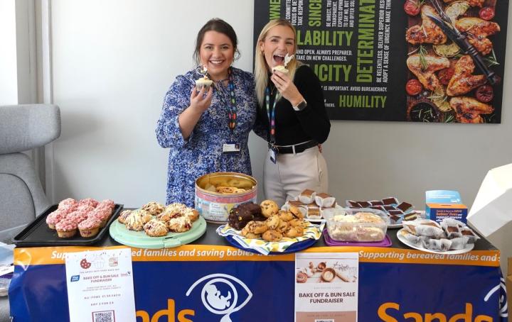 Company bake sale with employees eating cakes and Sands banners