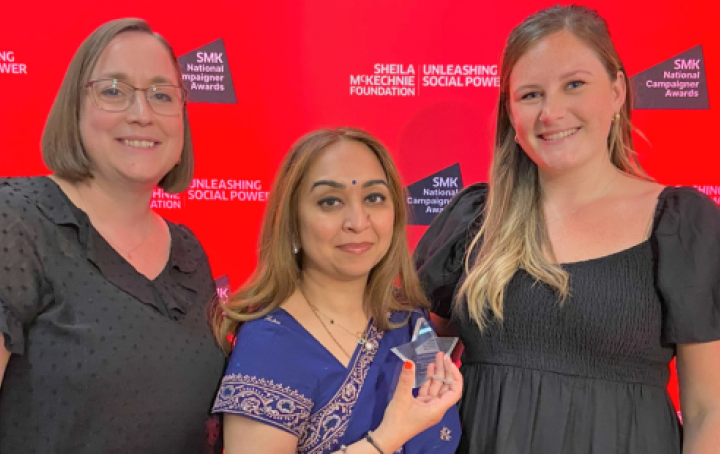 Three people holding an award at a ceremony and smiling