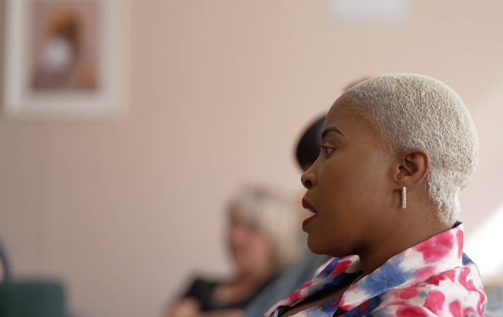 Black woman with short blonde hair and colourful blazer is seated