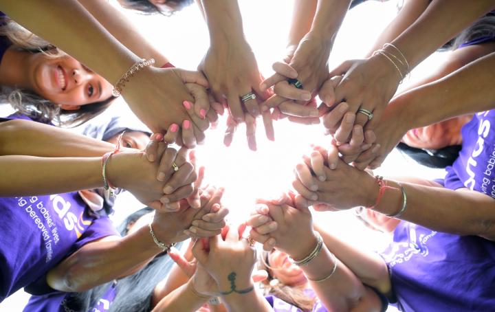 Ladies stood together putting their hands together and looking down towards the camera