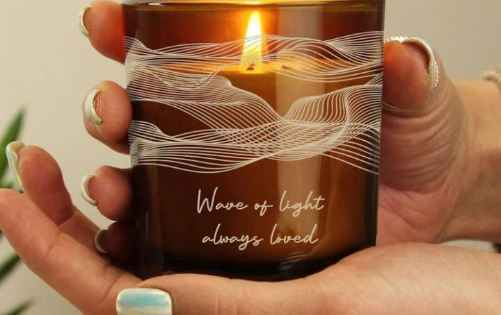 lit amber candle with words reading "wave of light, always loved"