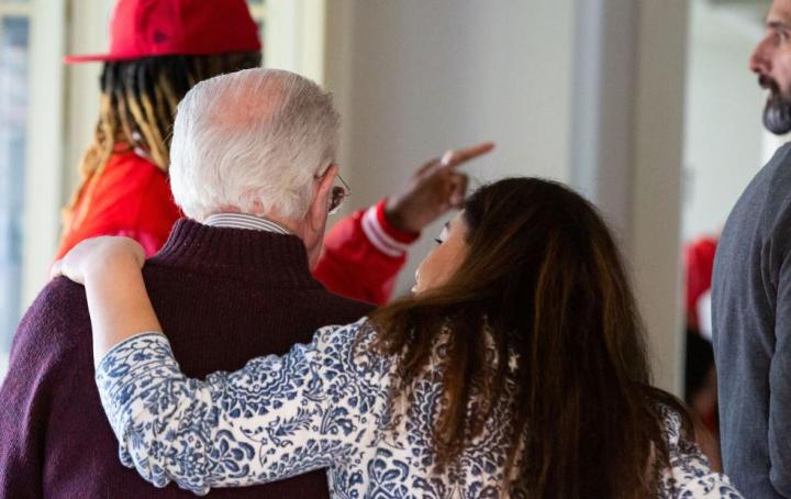 A lady has her arm around an older gentleman's back to give support