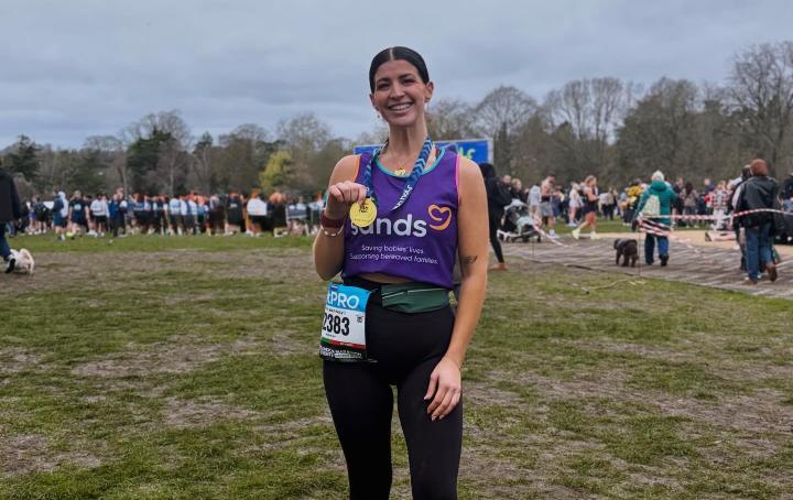 A woman standing in a field holding with her hand a medal.