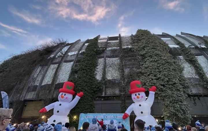 Building with greenery on it, Two snowman and a crowd of people.