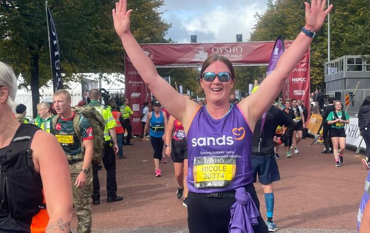 A woman standing up, with arms up in the air, after running a race,