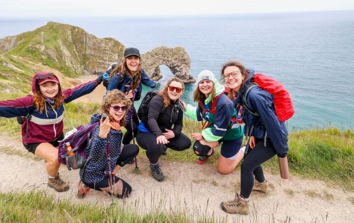 Six women on a path, with the sea and cliffs.